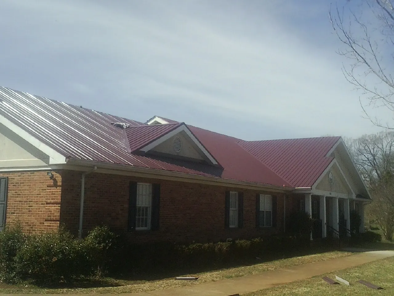 Red metal roof with gabled entries on a long brick building, from a Hail Damage Roof Repair job in Mount Carmel