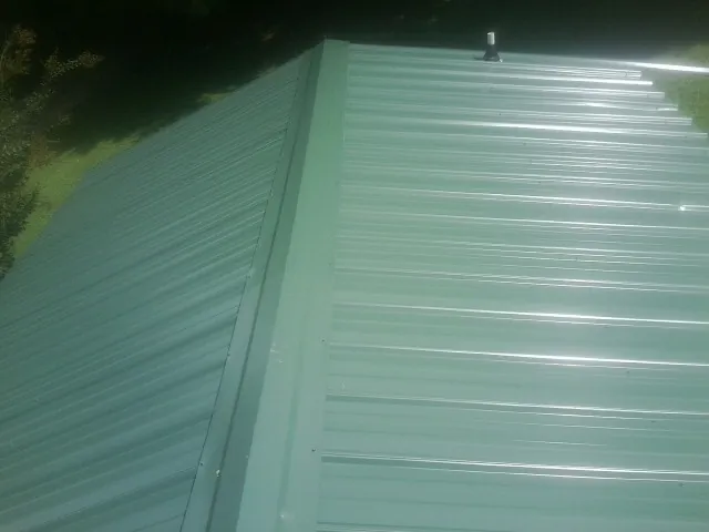 New green metal panels meeting at the ridge of a roof — Flat Roof Repair work by our crew in Mount Carmel