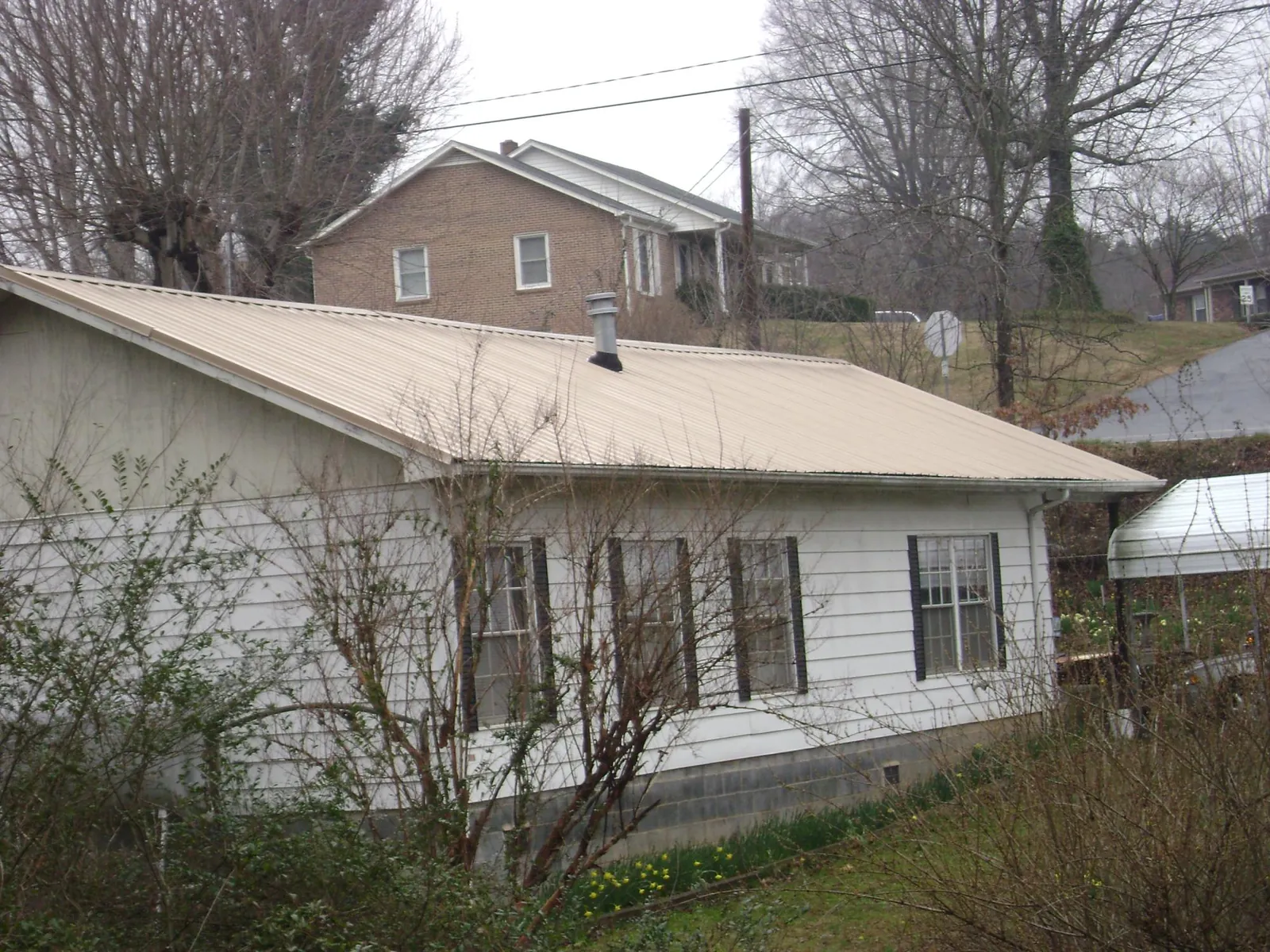 Tan metal roof on a white sided house set into a hillside — Commercial Roofing by Roofing Brothers in Mount Carmel